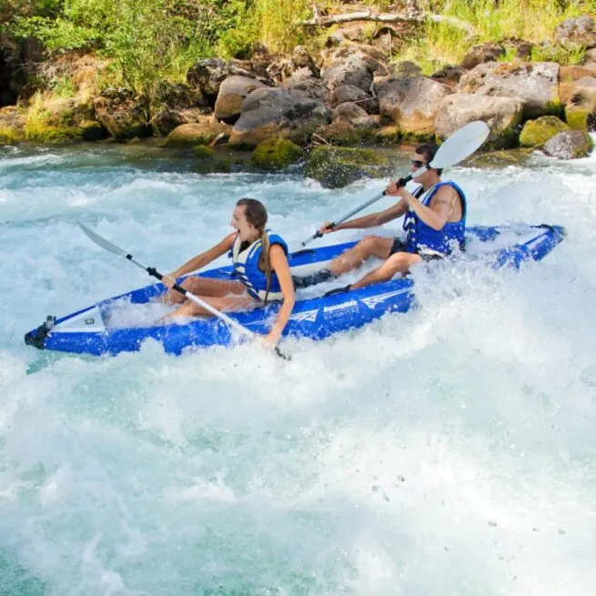 Aquaglide Klickitat inflatable two seat kayak in blue the whitewater with two people paddling.