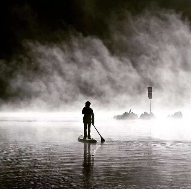 A black and white image of a paddleboarder paddling in the fog.
