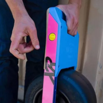 OneWheel XR Charger Port Plug in yellow with pink rail guards and hot blue bumpers.
