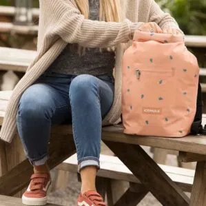 A girl sitting at a bench with the Jaunt sunset mule backpack style cooler.