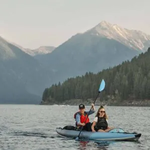 People paddling the new Aquaglide Chelan 155 inflatable touring kayak on a lake with beautiful snow covered mountains in the background.