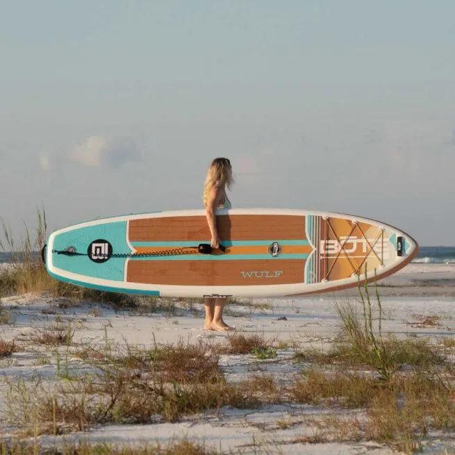 Woman with Bote Boards 11'4" Wulf Native Dune paddleboard on the beach at sunset. Riverbound Sports Paddle Company