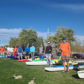 Group of people with paddleboards on grassy field. Tempe Town Lake Fitness Paddle.