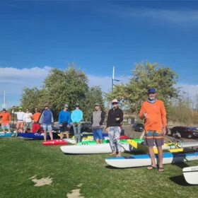 Group of people with paddleboards on grassy field. Tempe Town Lake Fitness Paddle.