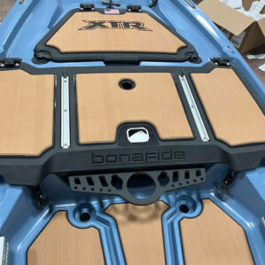 A top-down view of a black Bonafide XTR Tool Caddy mounted to the light blue deck of a kayak. The caddy is positioned directly below the